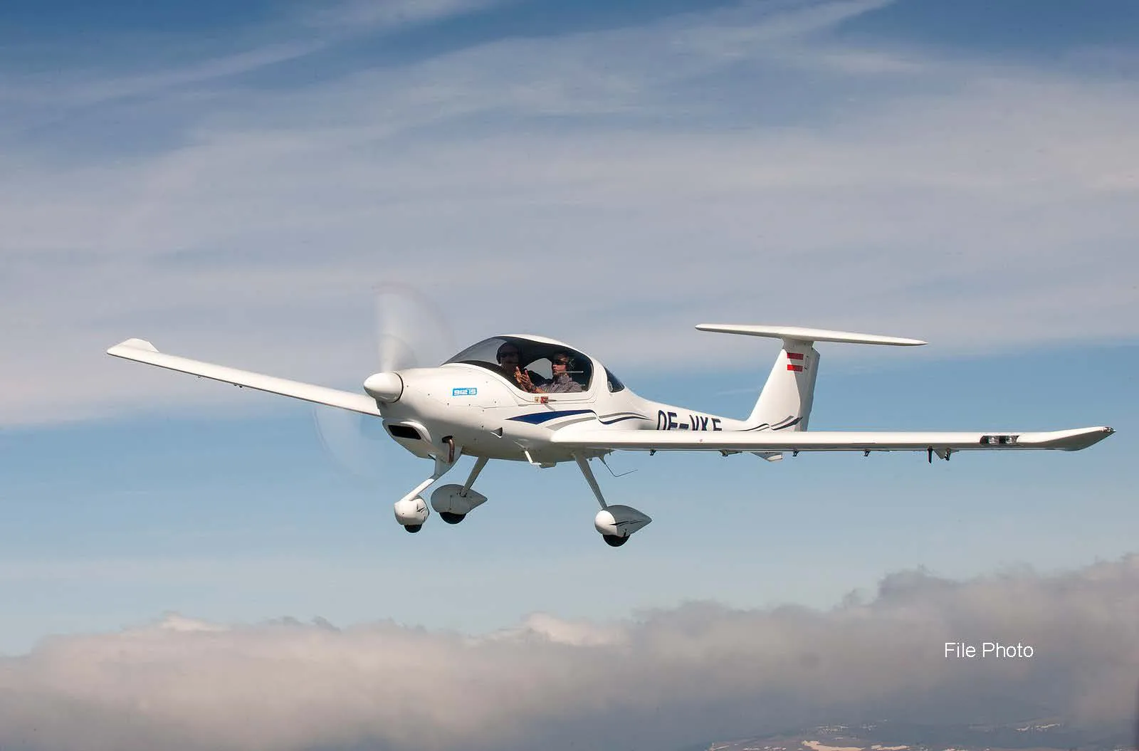 A white Diamond DA40 aircraft with blue stripes and registration OE-JYC flying in a blue sky with clouds.