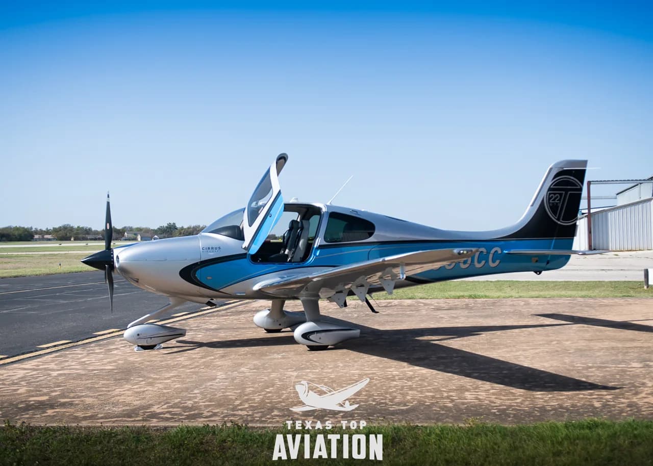 A Cirrus SR22 aircraft with blue and silver paint scheme parked on an airfield with its doors open.