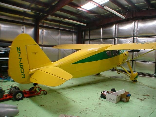 A yellow and green Fairchild 24 aircraft with registration N77603 inside a hangar.