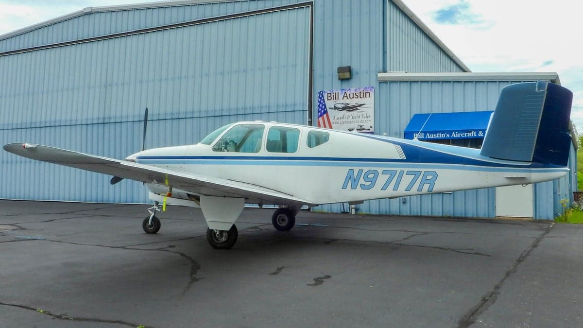 A white and blue Beechcraft Bonanza parked in front of a hangar.