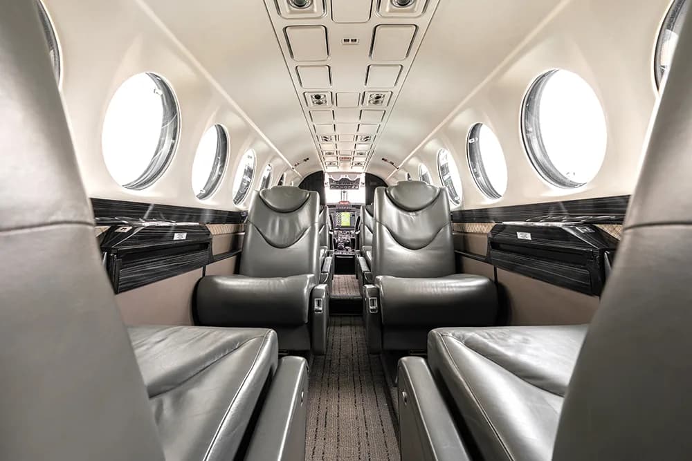 A view down the aircraft cabin aisle with grey leather seats and large circular windows.