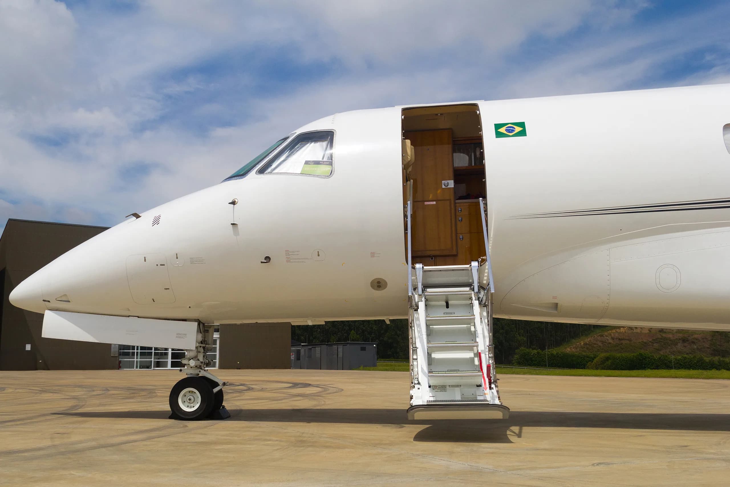 The front section of a white Embraer Legacy business jet with its main door open and stairs extended on the tarmac.