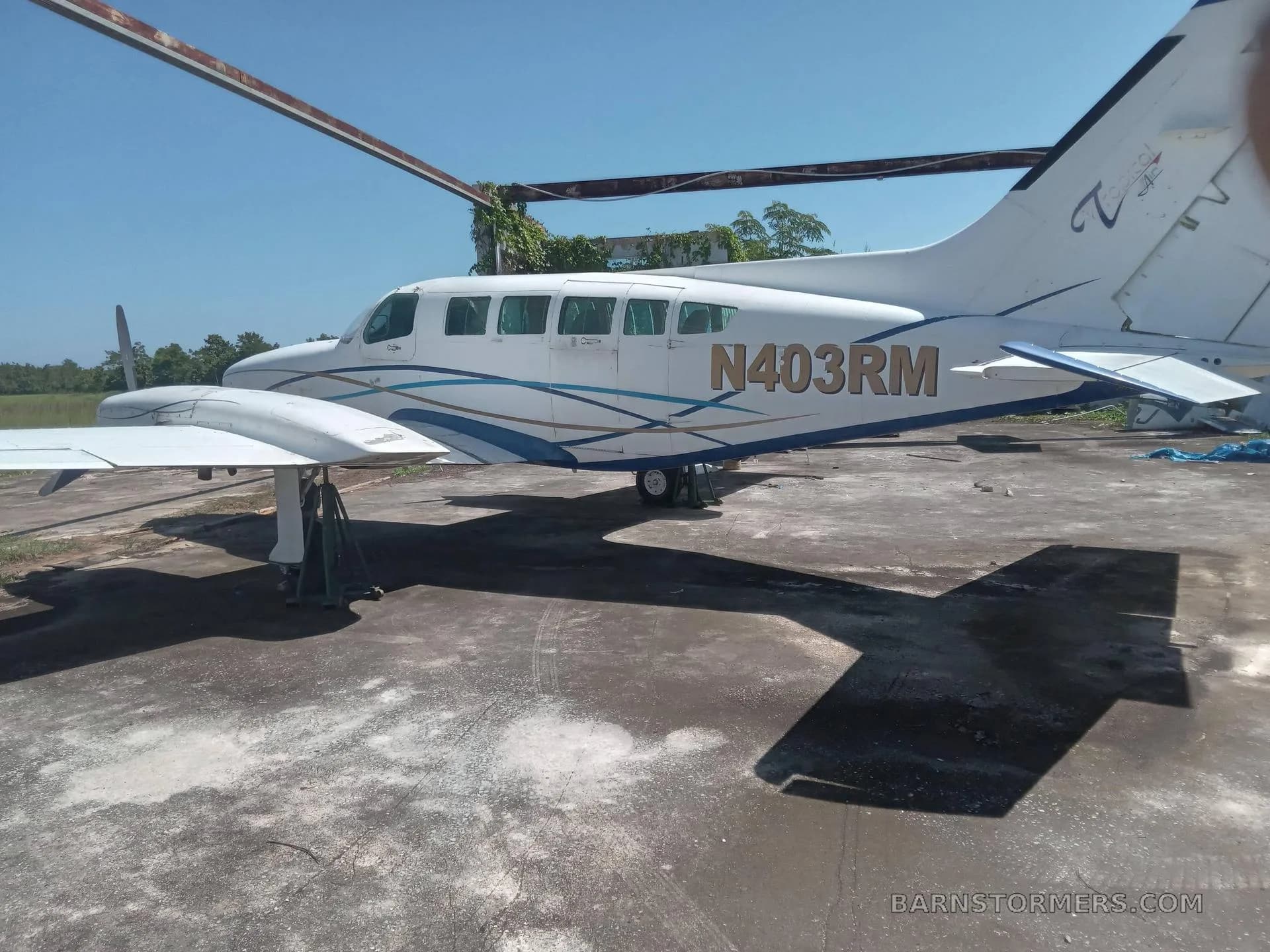 A white and blue twin-engine propeller aircraft with registration N403RM, parked on an asphalt surface under a clear blue sky, showing its full side profile.
