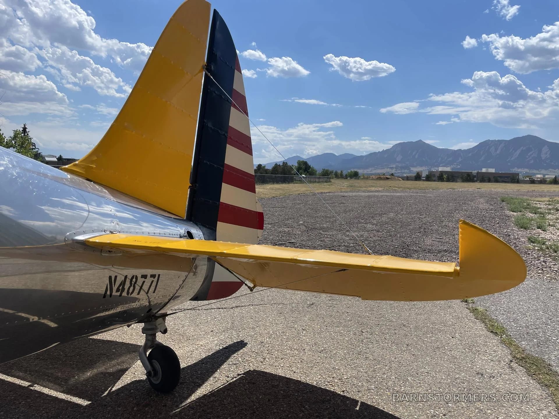 A close-up view of the tail section of a silver and yellow biplane, featuring a red, white, and blue striped rudder and registration N48771.