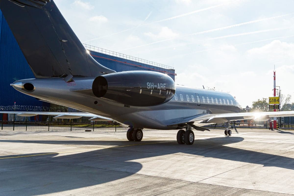 The tail section of the Bombardier Global 5000 aircraft 9H-ARE is shown on the tarmac with a gray and black paint scheme.