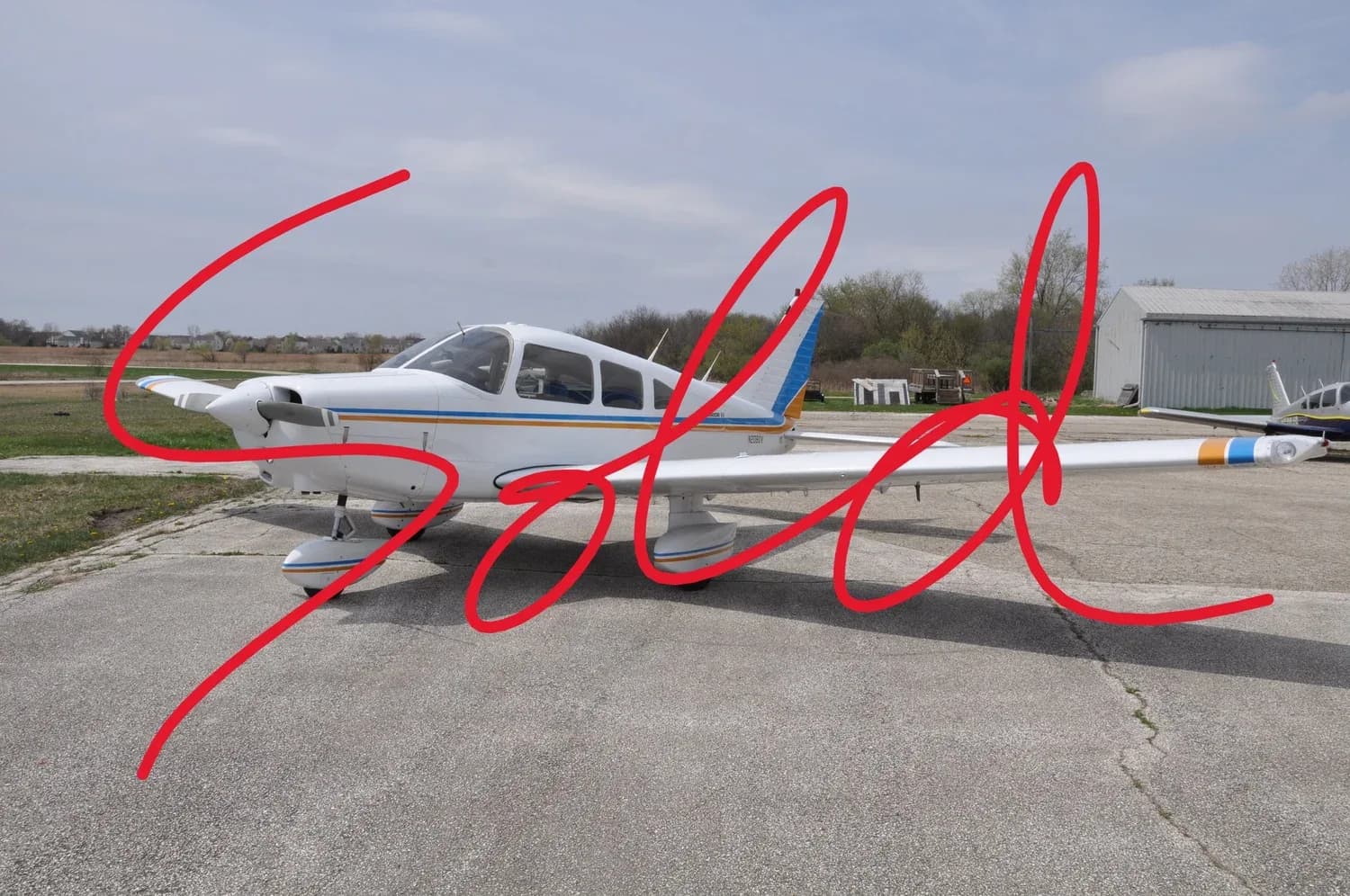 A white single-engine propeller aircraft with blue and orange stripes parked on an asphalt apron.