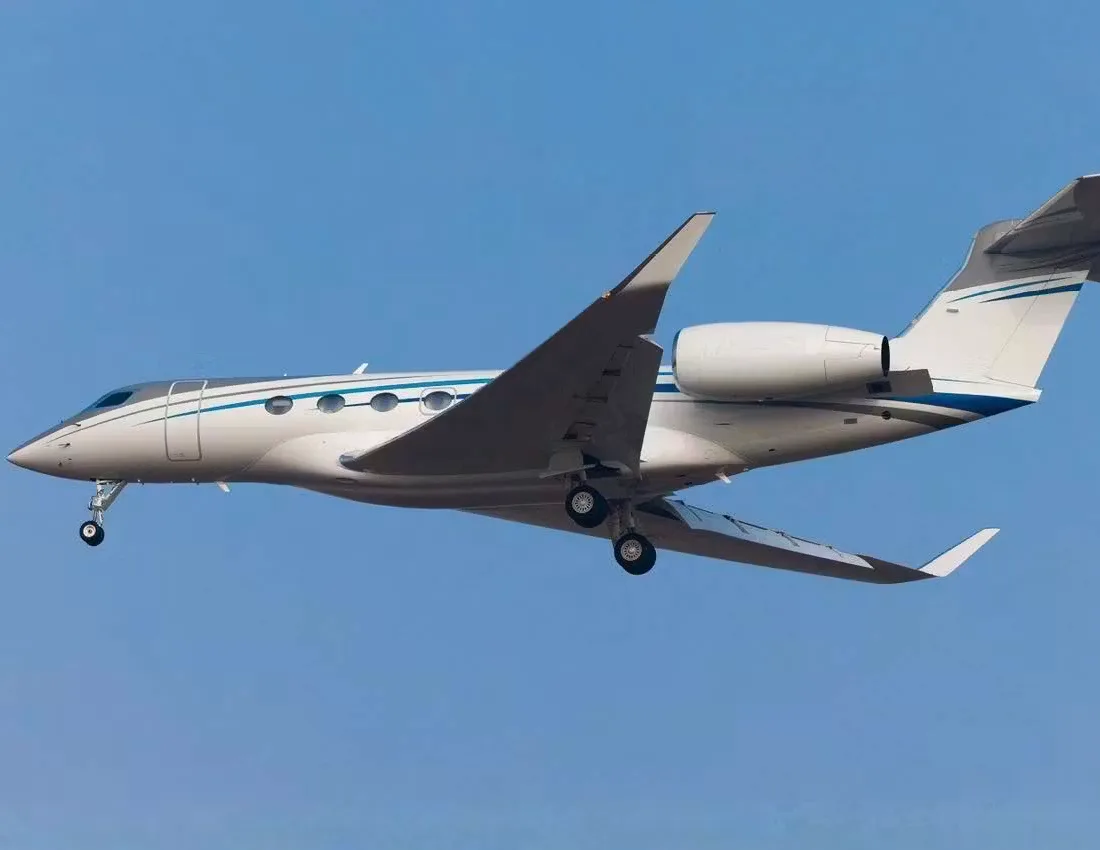 A white and silver Gulfstream business jet is in flight against a clear blue sky.