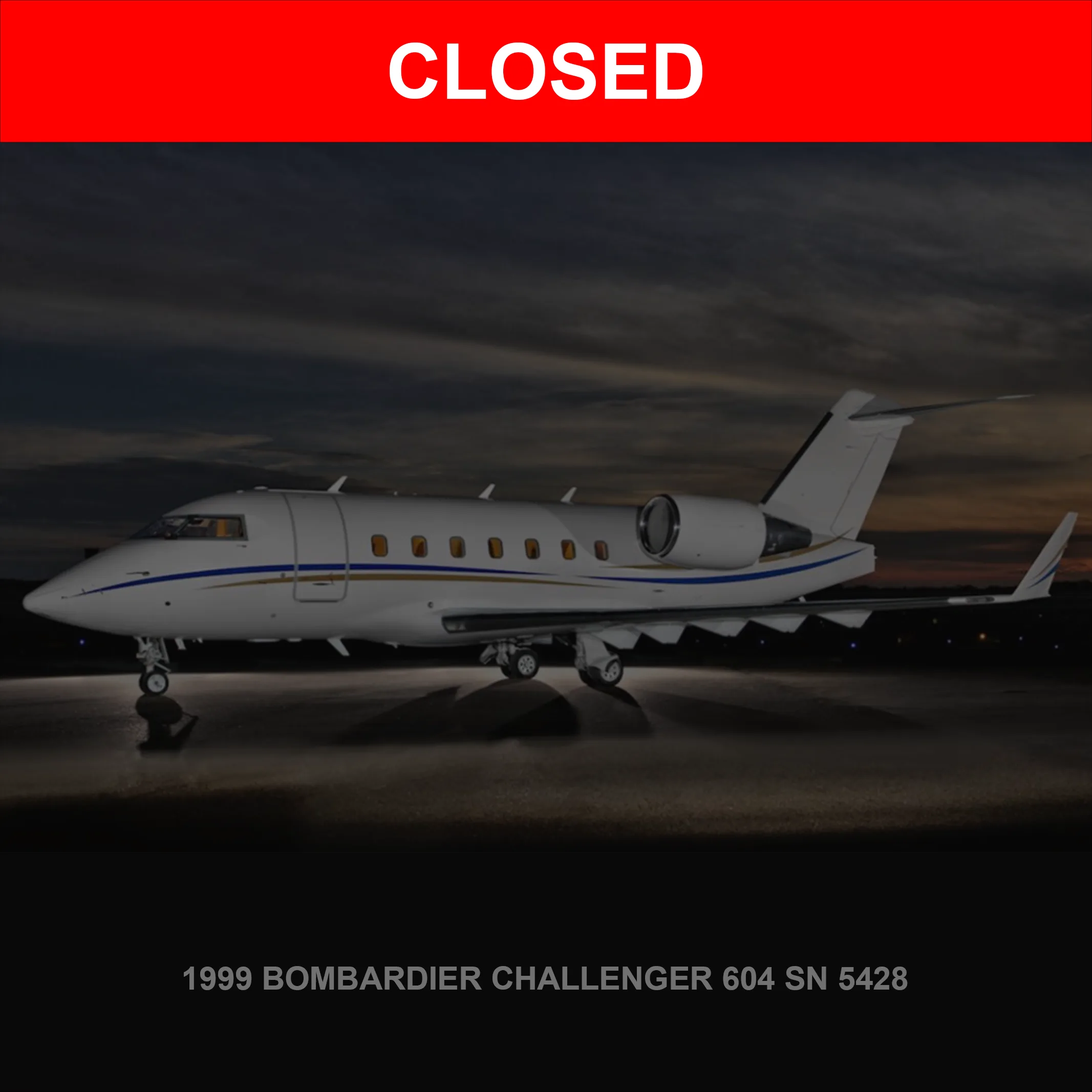 A white Bombardier Challenger 604 business jet with blue and gold stripes is parked on a wet tarmac at dusk.