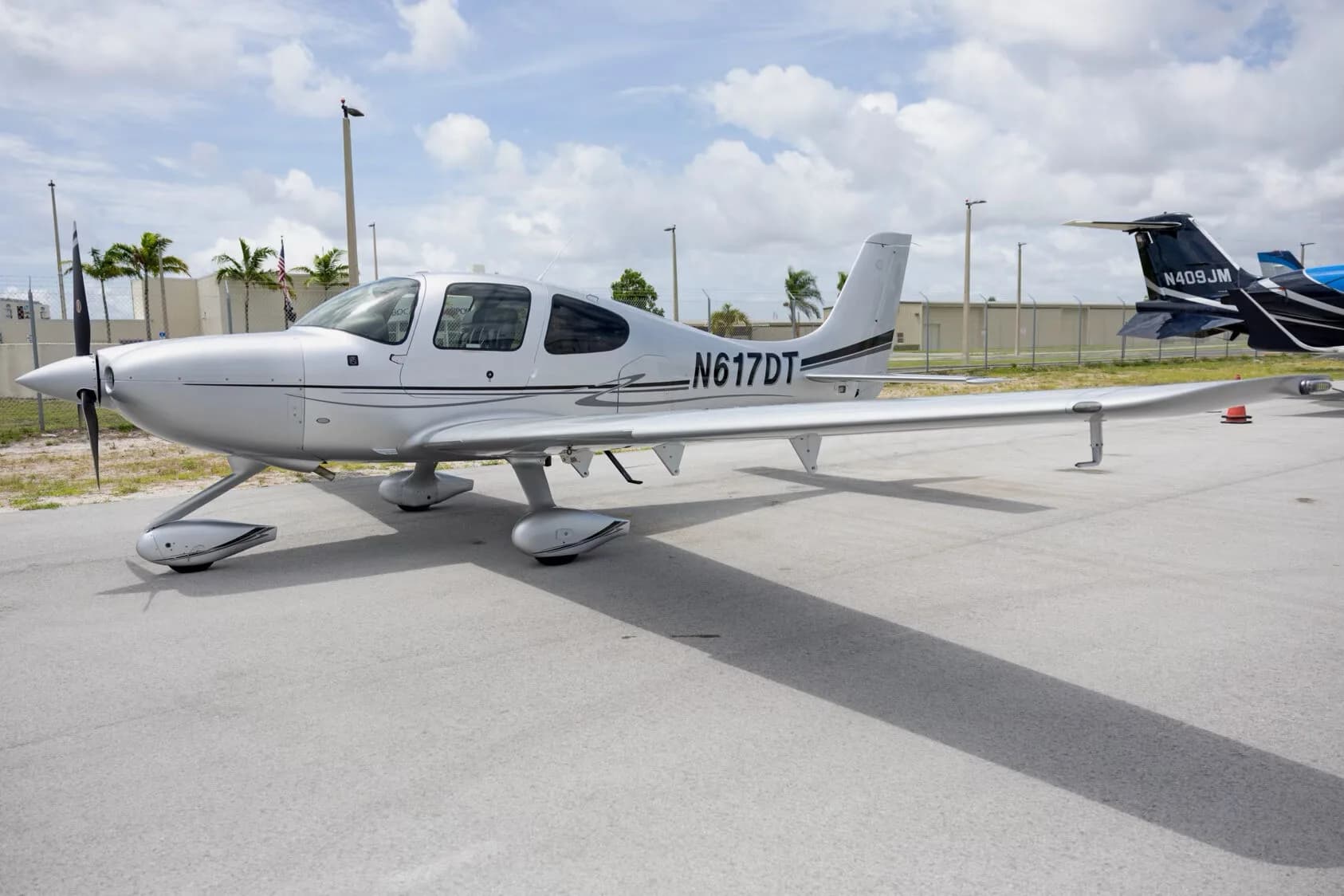 A silver Cirrus SR22 aircraft with tail number N617DT parked on an tarmac with another aircraft in the background.