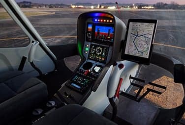 Helicopter cockpit with a digital instrument panel and tablet displaying a map at dusk.