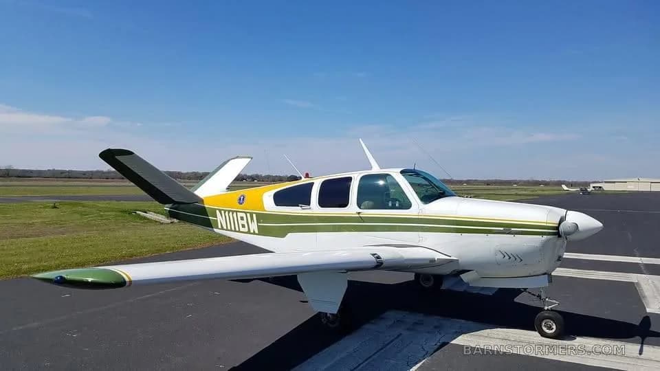 A green, white, and yellow single-engine propeller aircraft (N111BW) parked on a tarmac under a clear blue sky.