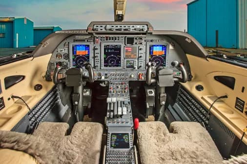 The cockpit of an aircraft featuring multiple digital displays, control yokes, and a central throttle quadrant.