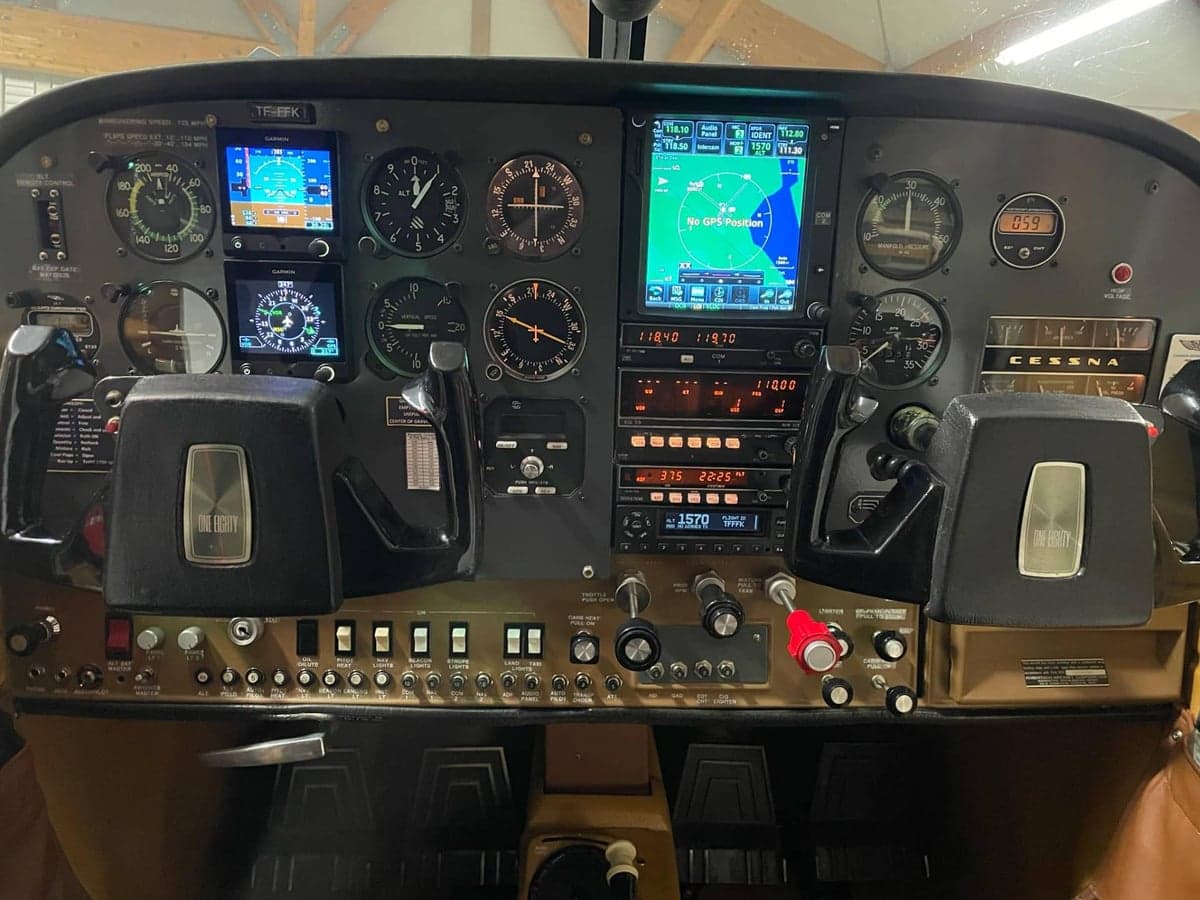 The full instrument panel of a Cessna 180 cockpit, featuring both analog gauges and modern Garmin displays.