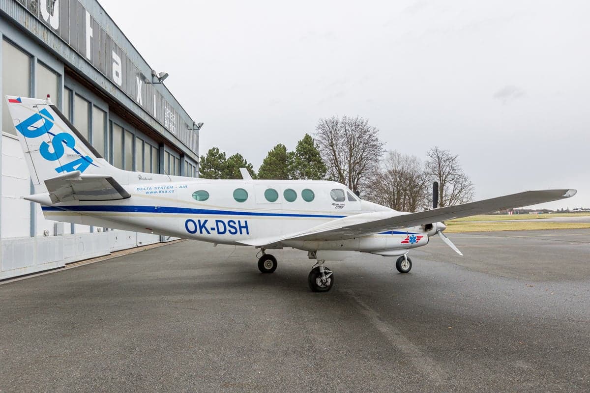 Side view of a Beechcraft King Air C90 aircraft with a white and blue paint scheme, parked on the tarmac.