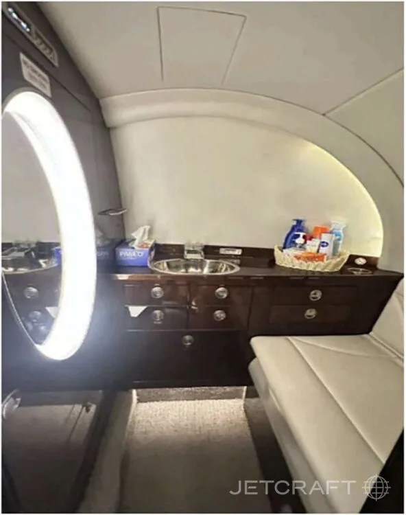 A lavatory or galley area features a sink, dark wood cabinetry, and a large illuminated mirror.