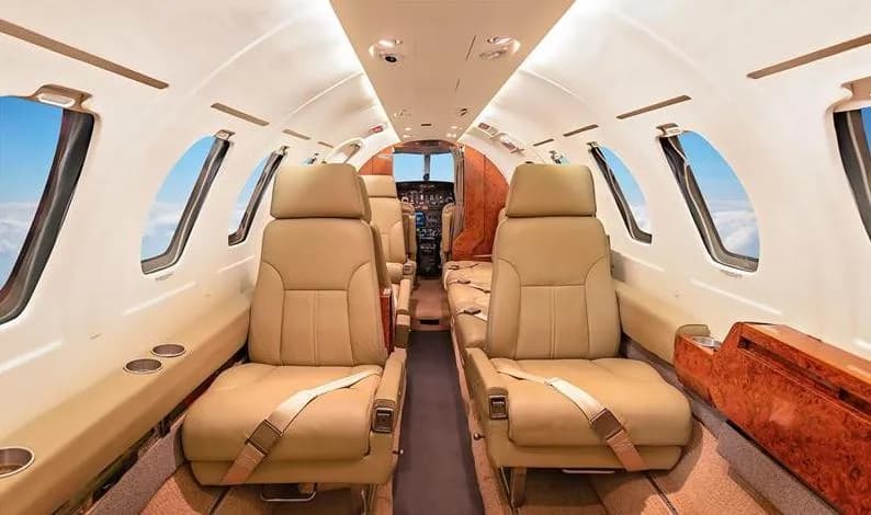 The interior cabin of a business jet with tan leather seats and wood accents, looking towards the cockpit.