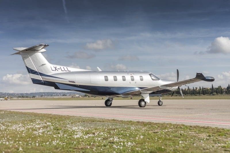A Pilatus PC-12 aircraft with registration LX-LLL parked on the grass.