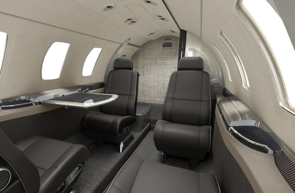 The interior of a Citation M2 aircraft with dark leather seats and a table.