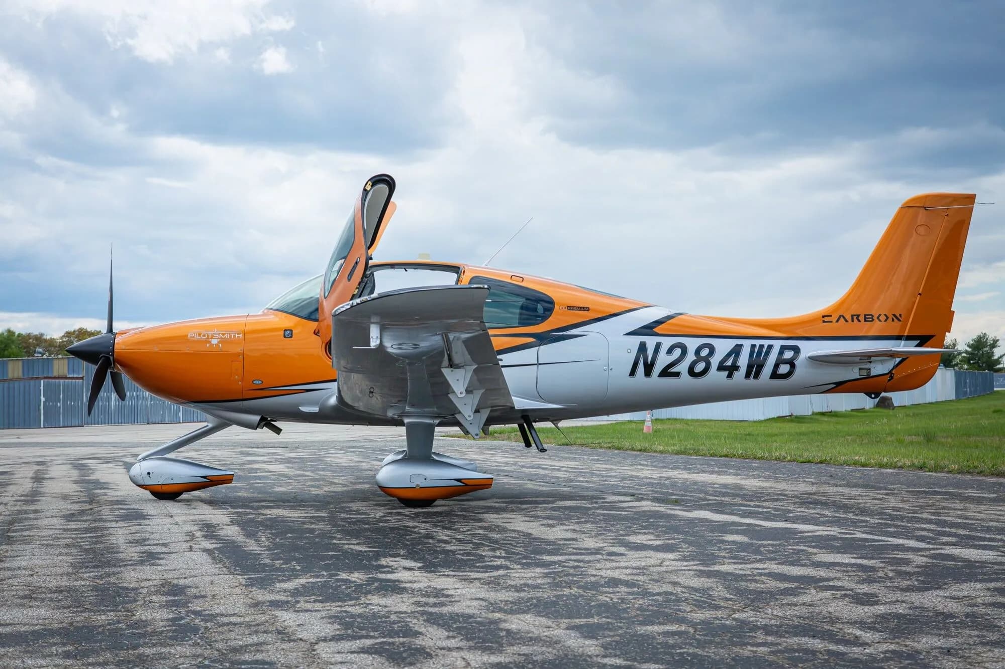 A side view of an orange and silver Cirrus SR20 aircraft, N284WB, with the pilot's door open on an airfield.