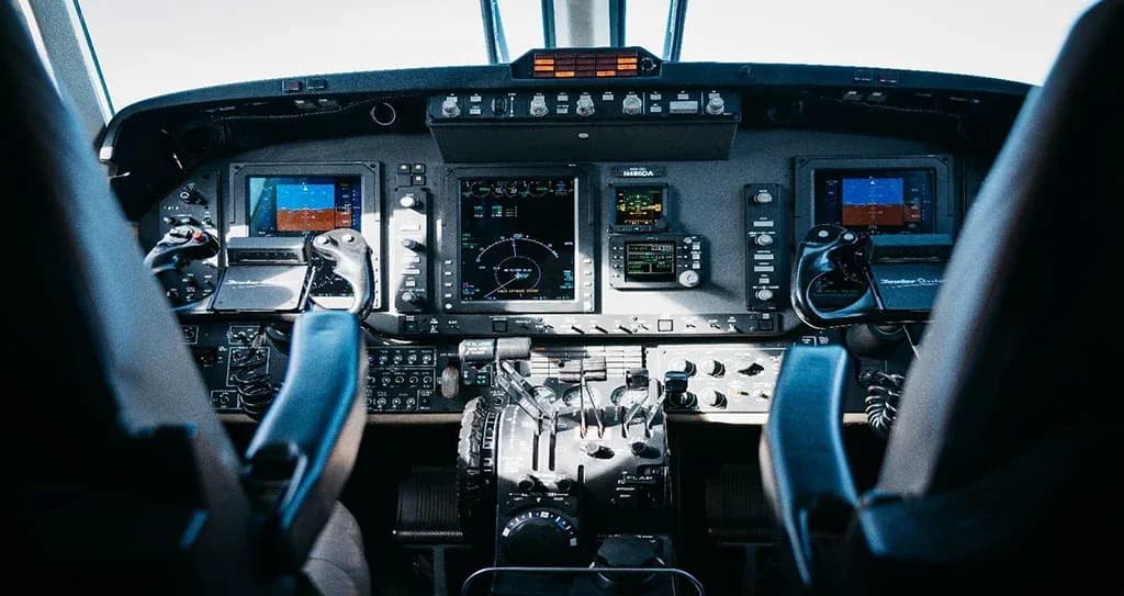 The aircraft cockpit with multiple digital displays, controls, and two pilot seats.