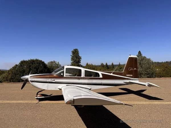 A brown and white Grumman American AA-5 Traveler aircraft (N4543A) is parked on an asphalt surface under a clear blue sky.