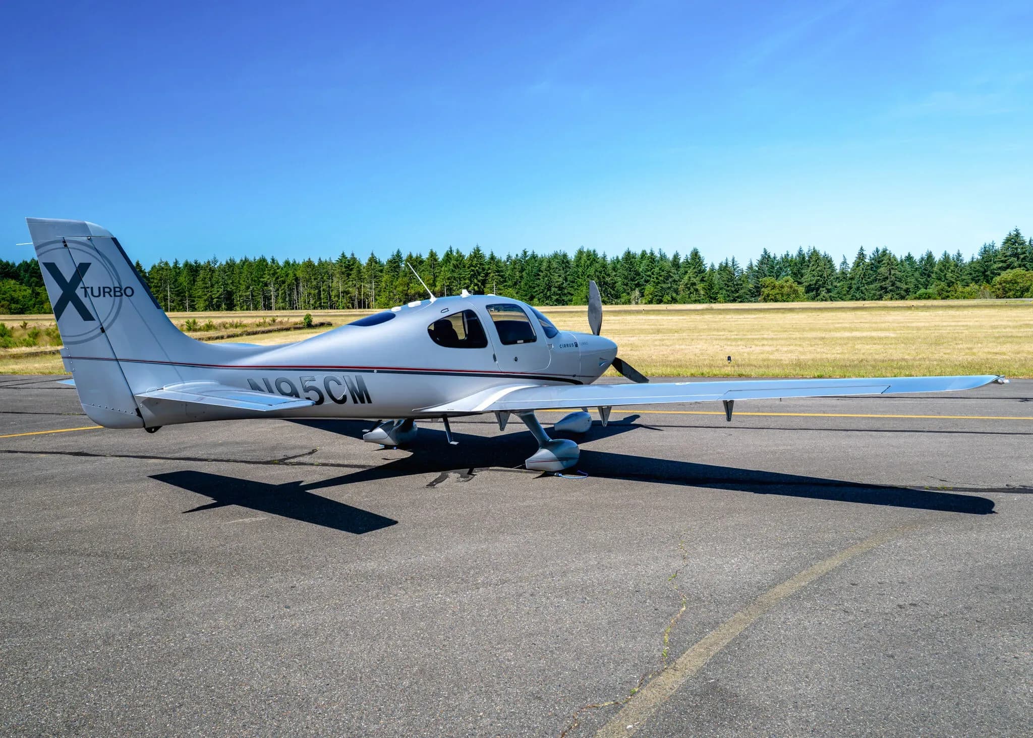 A silver Cirrus SR22T aircraft with registration N95CM parked on an airfield, viewed from a wider rear-side angle.