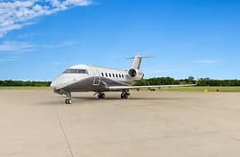 A gray and white private jet parked on a runway under a blue sky.