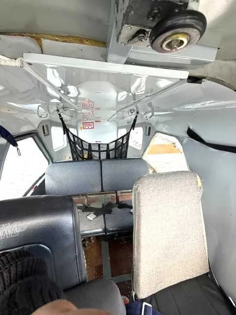 The interior cabin of an aircraft with multiple seats and a cargo net visible towards the rear.