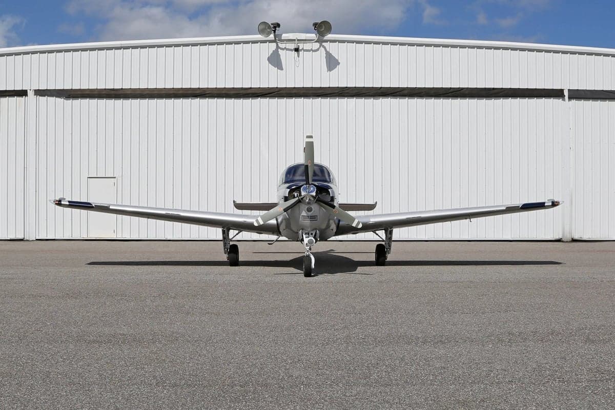 Front view of a Beechcraft Bonanza aircraft parked on the tarmac in front of a hangar.