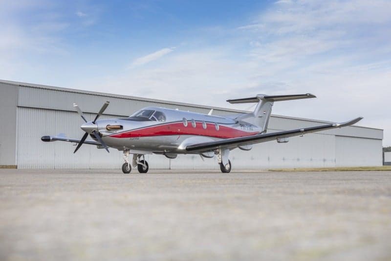 A Pilatus PC-12 aircraft with a silver and red paint scheme, registration PH-PNG, parked in front of a hangar.