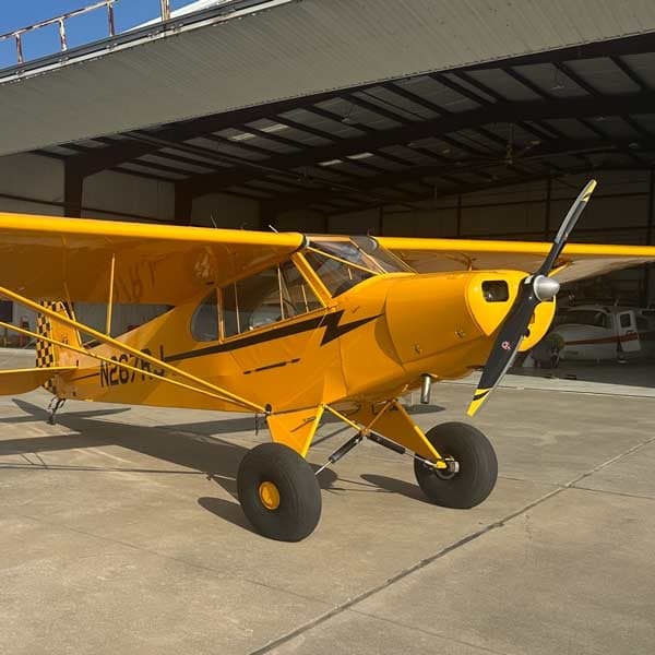 Three-quarter front view of a yellow Legend Cub aircraft with registration N267RJ, parked outside a hangar.