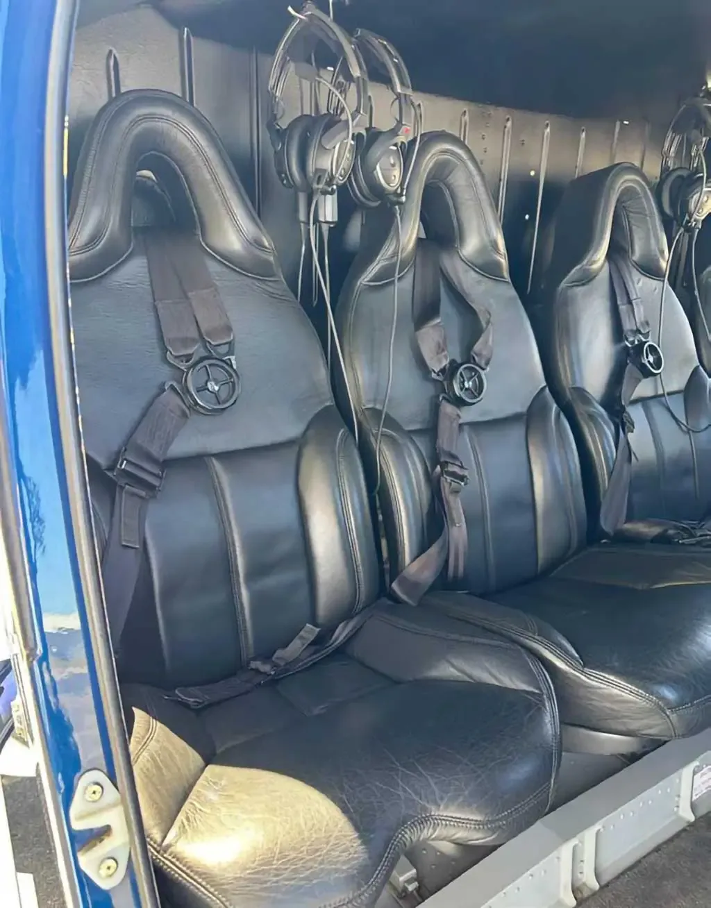 A closer view of the helicopter's interior, showing three black leather seats with safety harnesses and headsets.