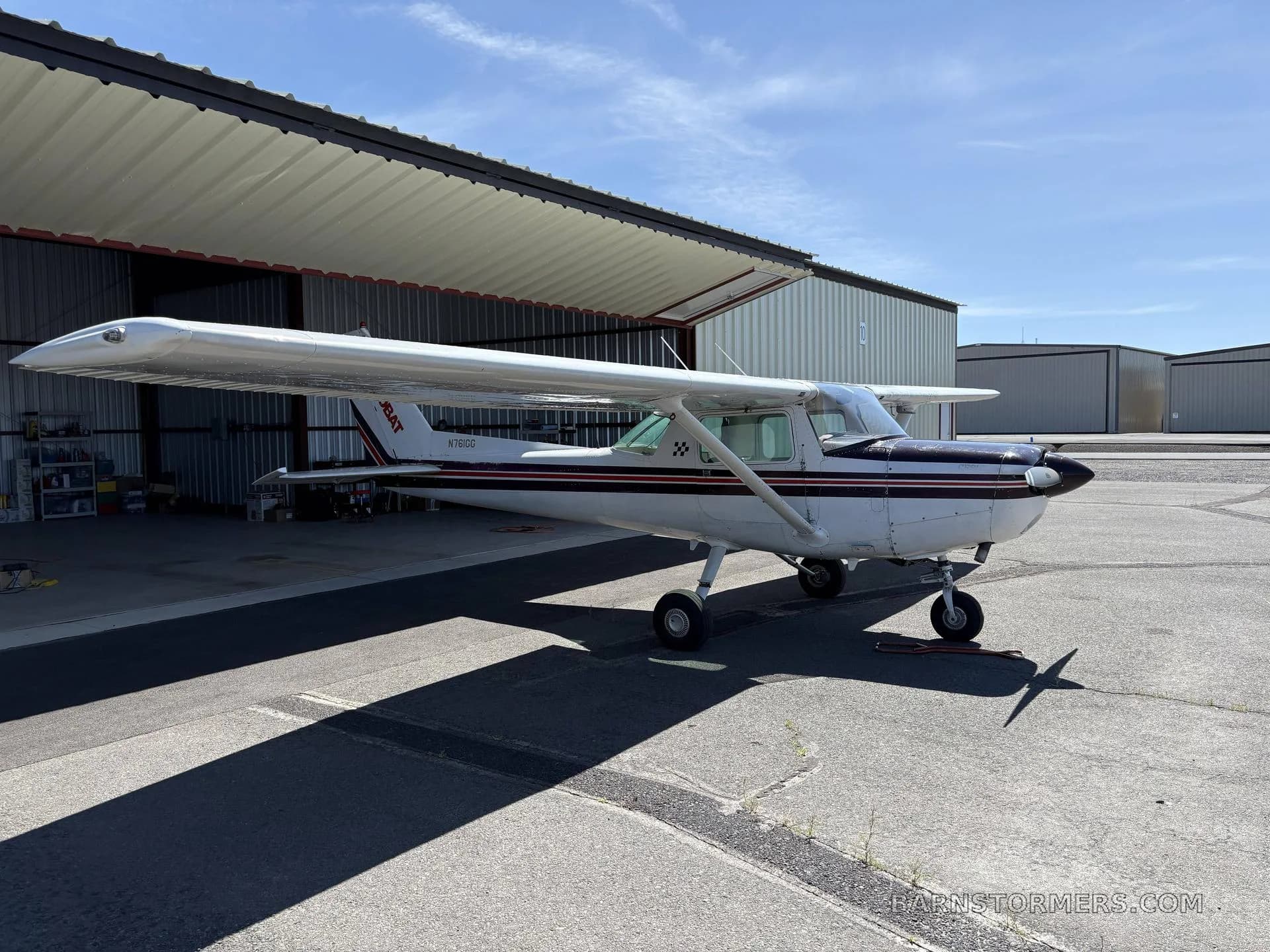 A front-quarter view of a white and maroon Cessna 150 Aerobat (N761GG) parked on an asphalt apron.