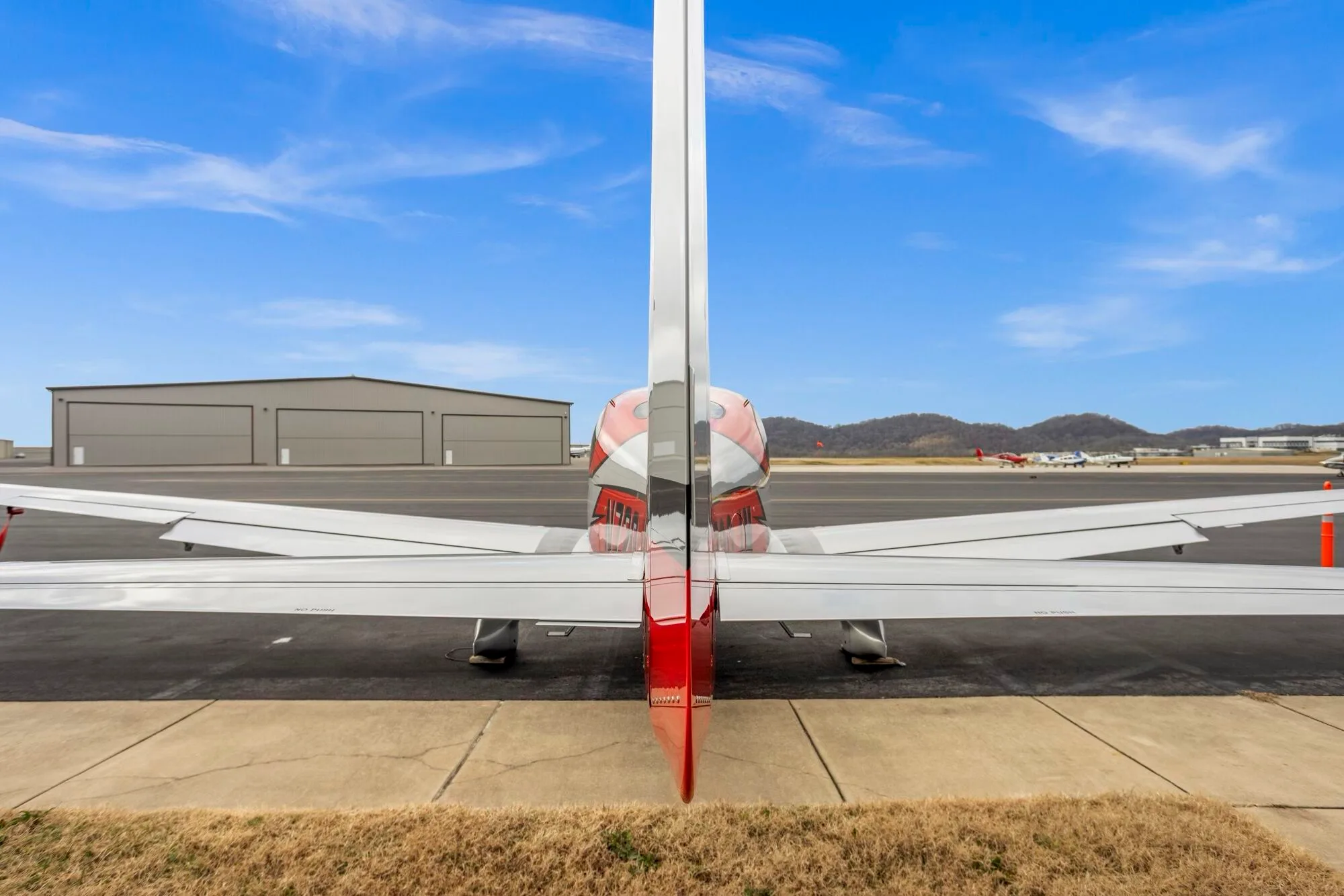 A rear view of a red and silver Cirrus SR22 aircraft parked on an airport tarmac.
