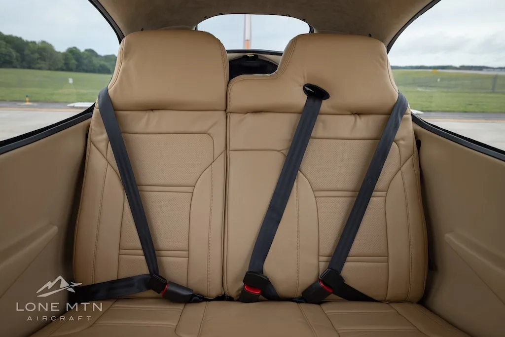 A straight-on view of the tan leather rear seats with seatbelts in the aircraft cabin.