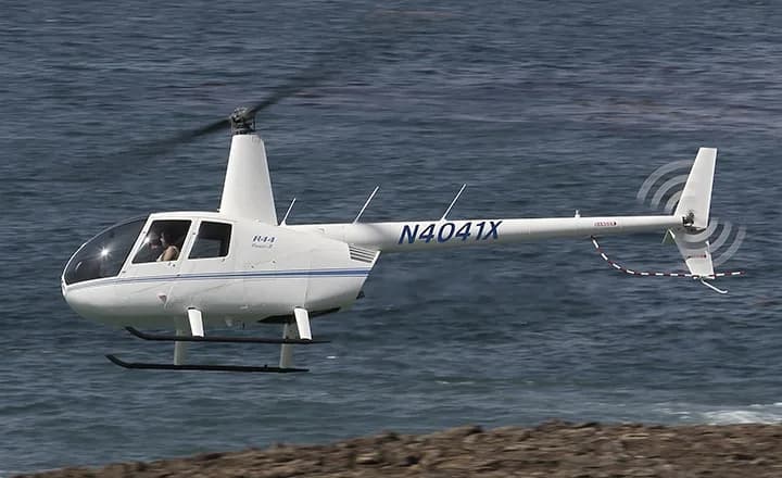Robinson R44 helicopter flying near the ocean.