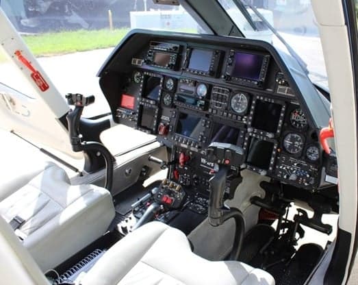 The cockpit of the Agusta Grand helicopter with white seats and a black instrument panel.