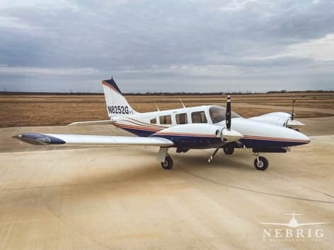 A white twin-engine propeller aircraft with blue and red stripes is parked on a tarmac under a cloudy sky.