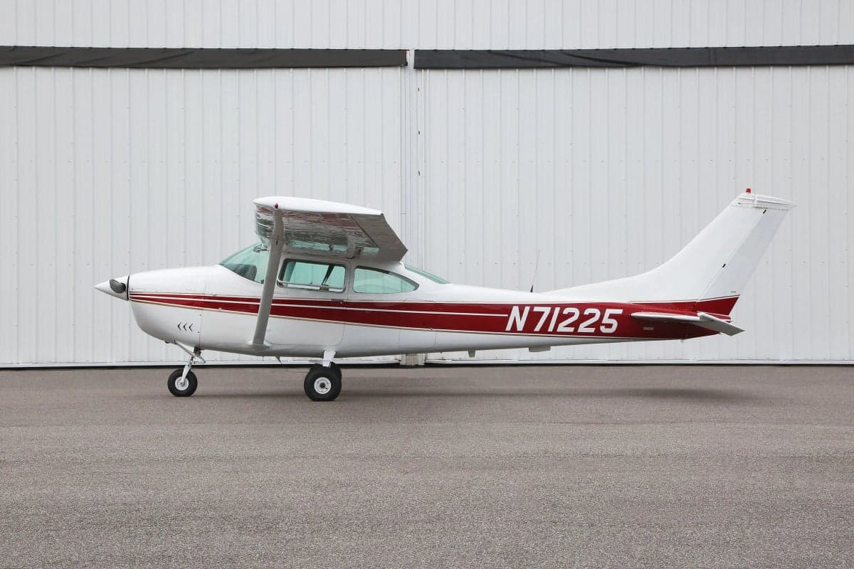 Side view of a Cessna aircraft with a white and red paint scheme parked in front of a hangar, showing the tail number N71225.
