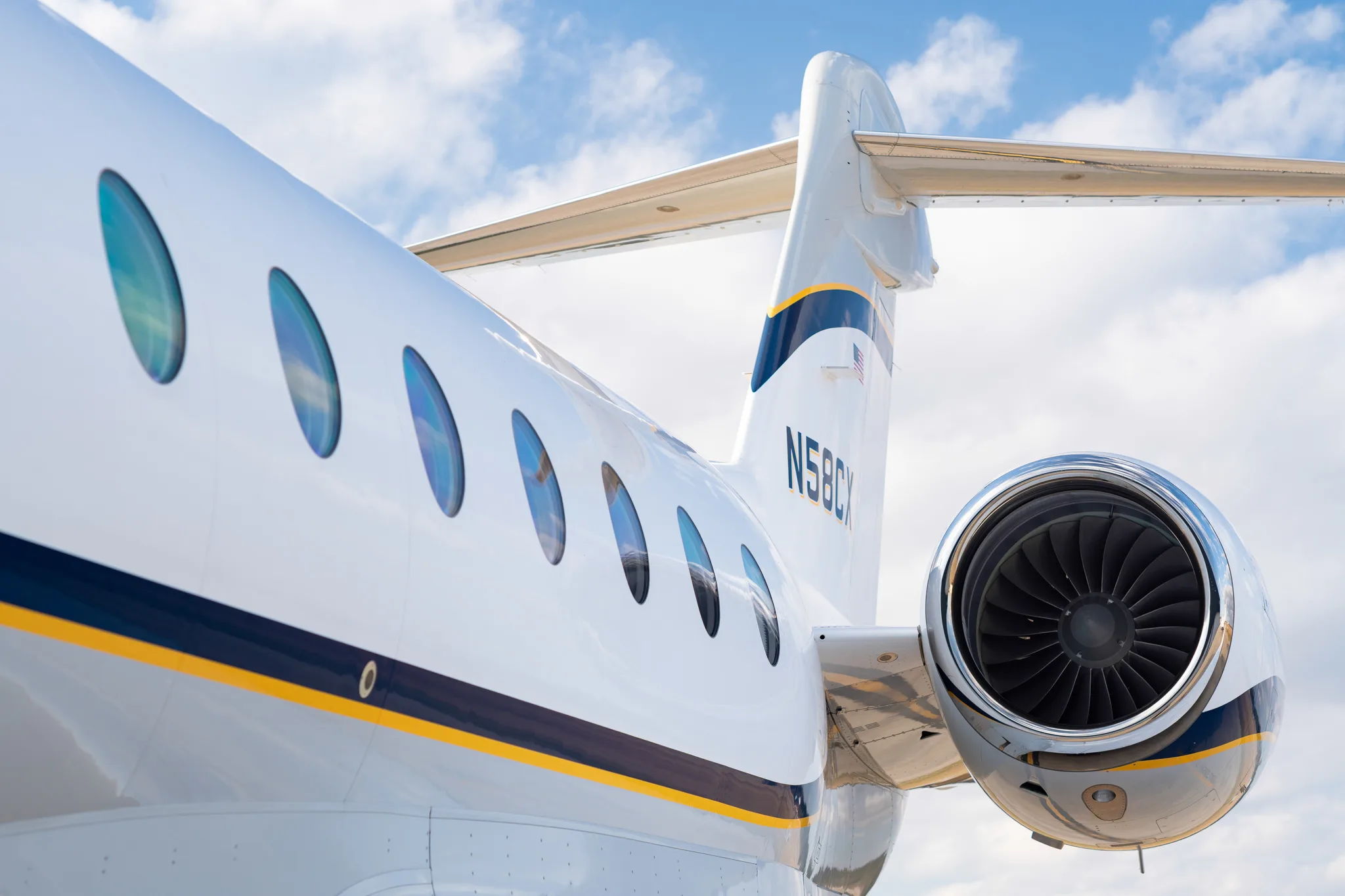 A close-up view of the rear fuselage and engine of a white business jet with blue and gold stripes, showing registration N58CX.