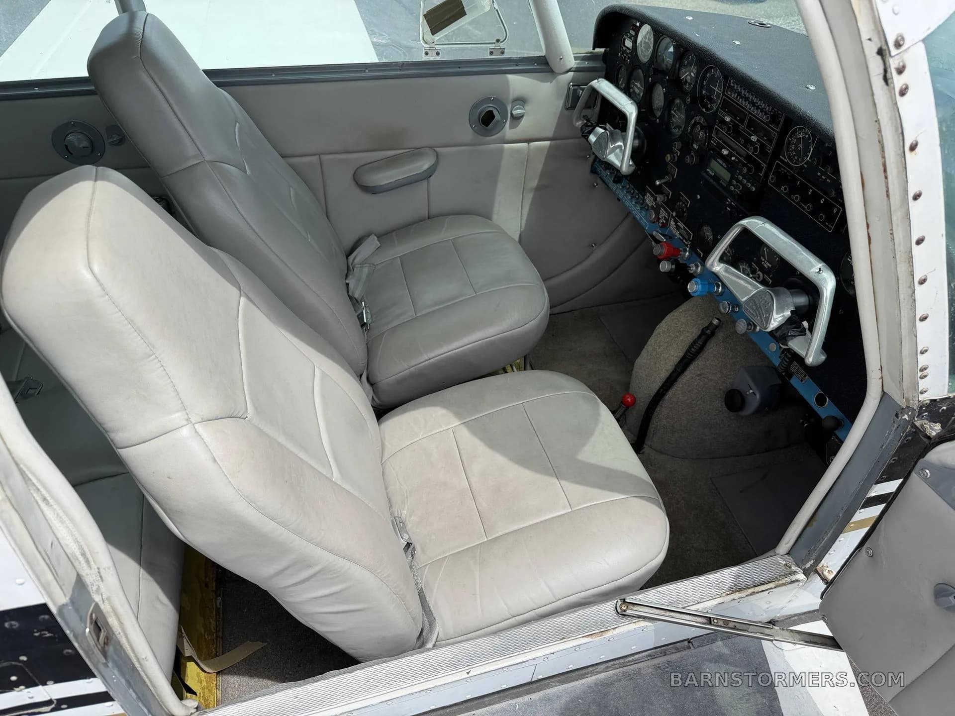 The light gray leather front seats of a small aircraft, with a view of the cockpit controls on the right.