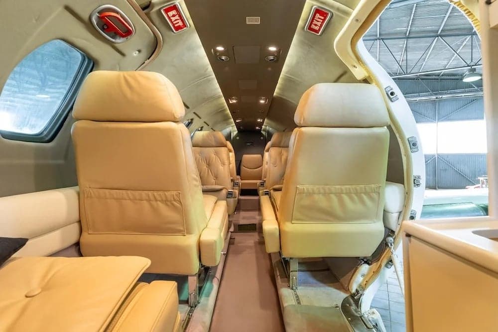 The interior of a Cessna Citation II features tan leather seats and an exit sign.
