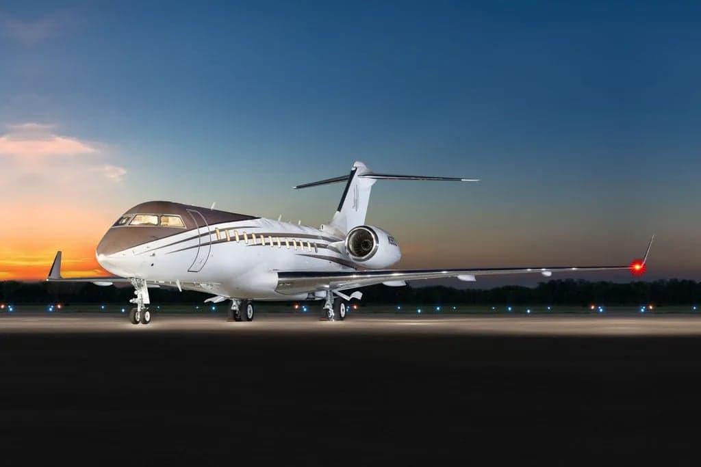 A Bombardier Global Express aircraft with a brown and white paint scheme on the tarmac at sunset.