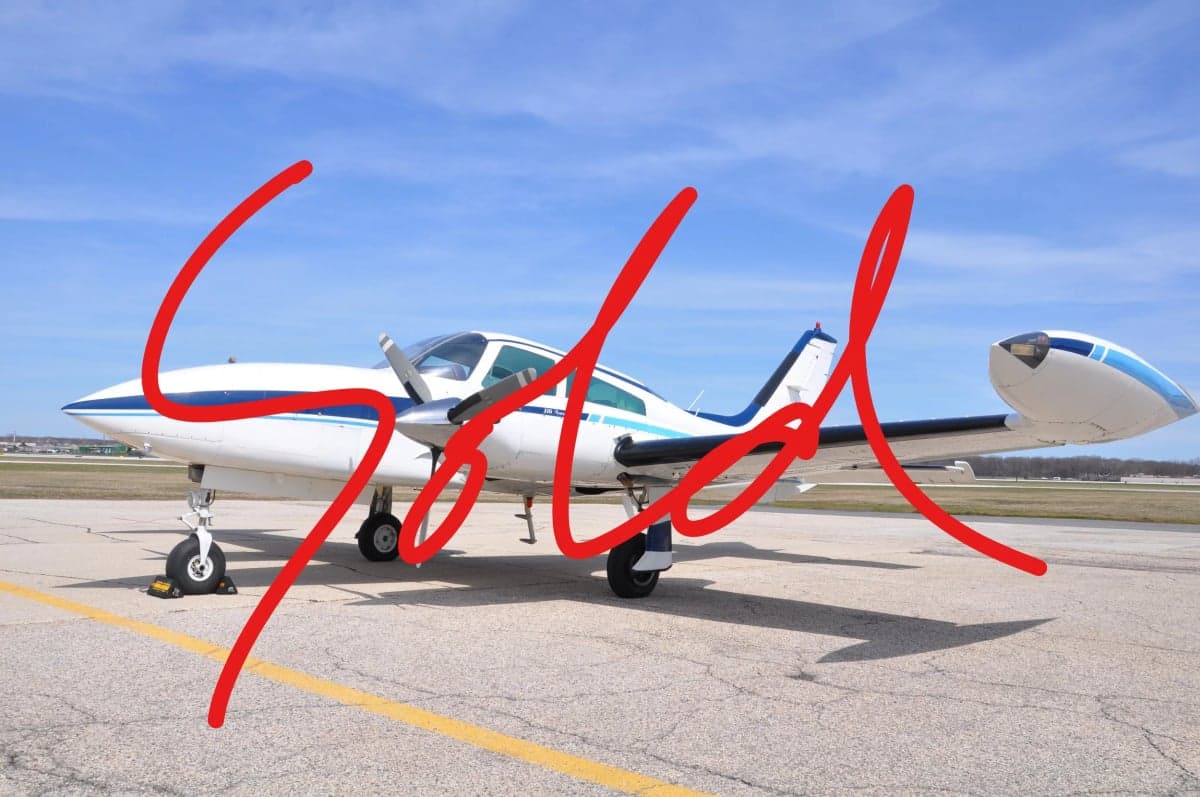 Side view of a white and blue Twin Commander aircraft with SOLD overlaid.