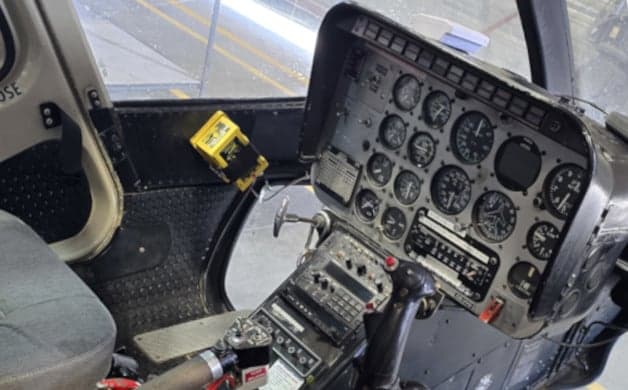 The cockpit of a helicopter shows the instrument panel with multiple gauges and controls.