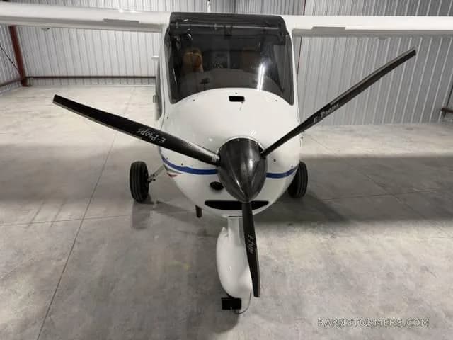 A front view of a white CTLS light sport aircraft with a black propeller, parked in a hangar.