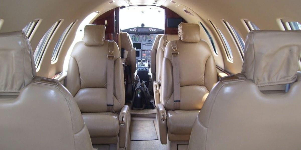 The interior cabin of a private jet, featuring tan leather seats and a view into the cockpit.