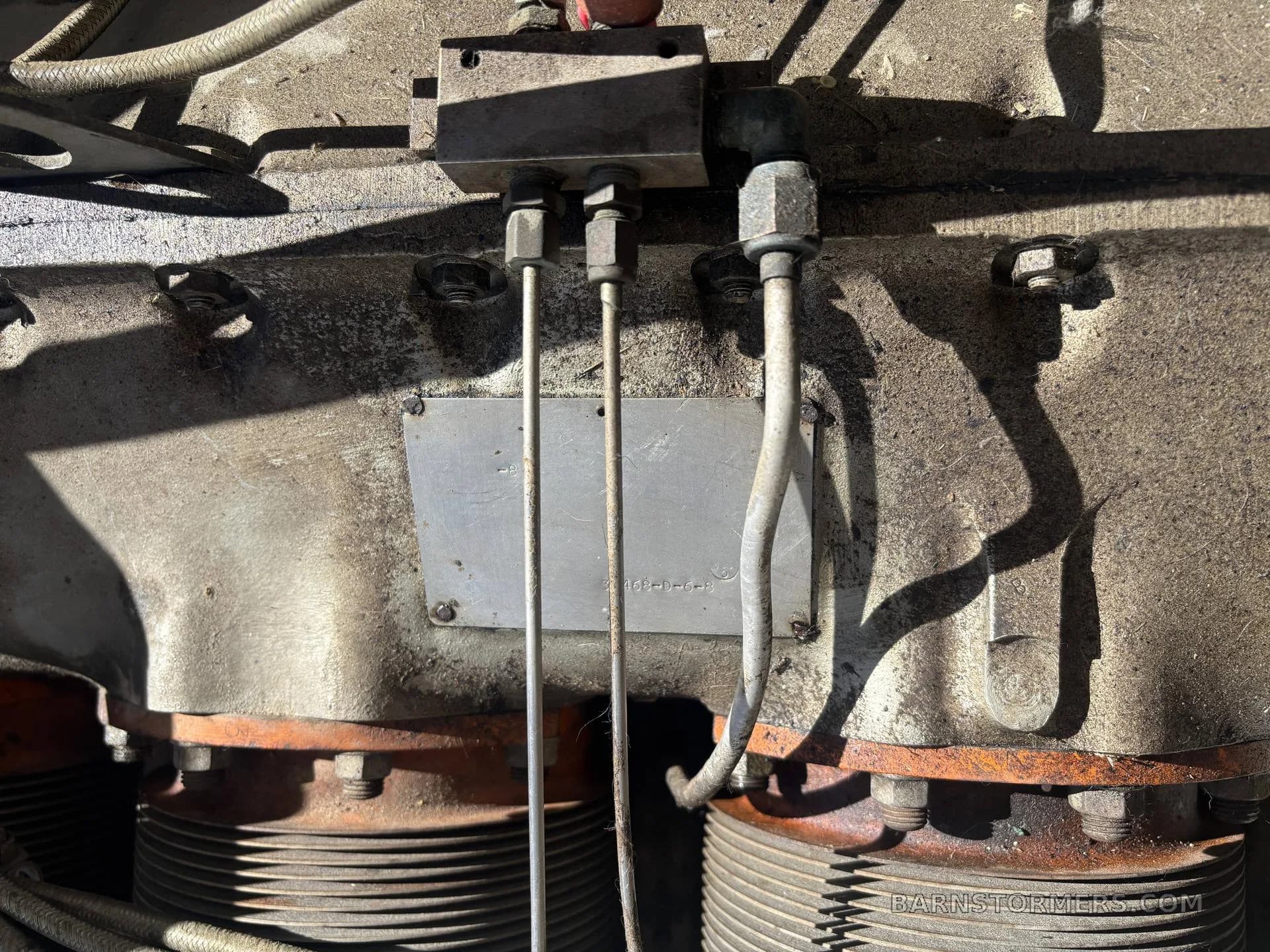 An extreme close-up of an aircraft engine's cylinders and connecting pipes, showing a metal identification plate.