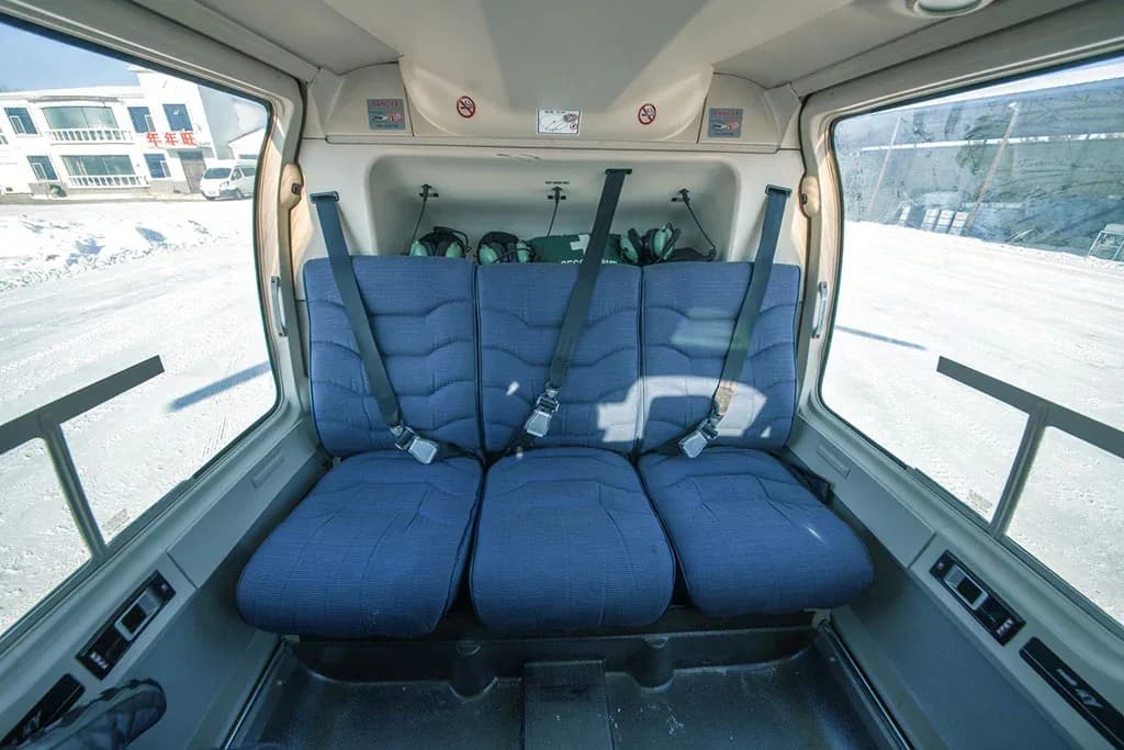 The rear cabin of the helicopter showing three blue seats with harnesses.
