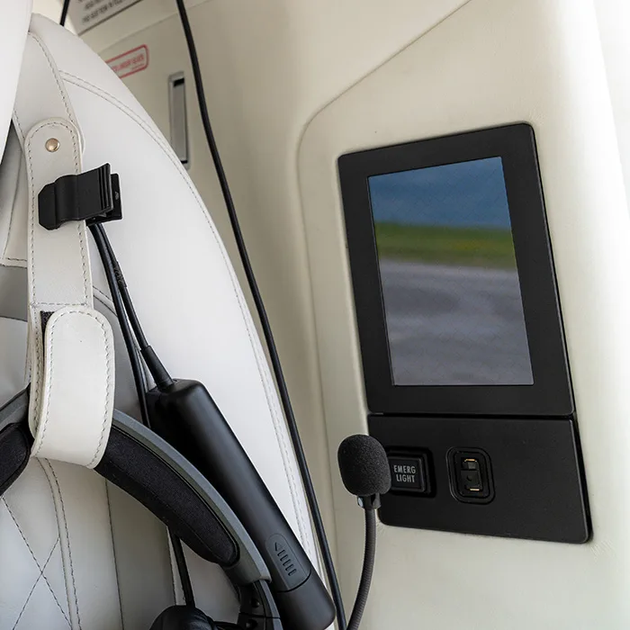 Close-up of a white leather seat with a headset and a small screen on the wall.